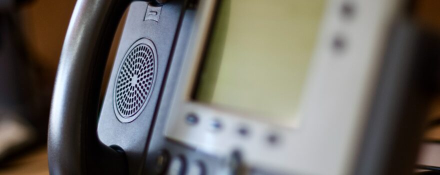 Close-up of a business desk phone highlighting speaker and display, representing VoIP vs landline discussion.