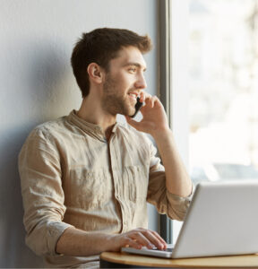 joyful attractive shaved guy sitting coworking space working laptop computer talking phone with girlfriend about date evening 1